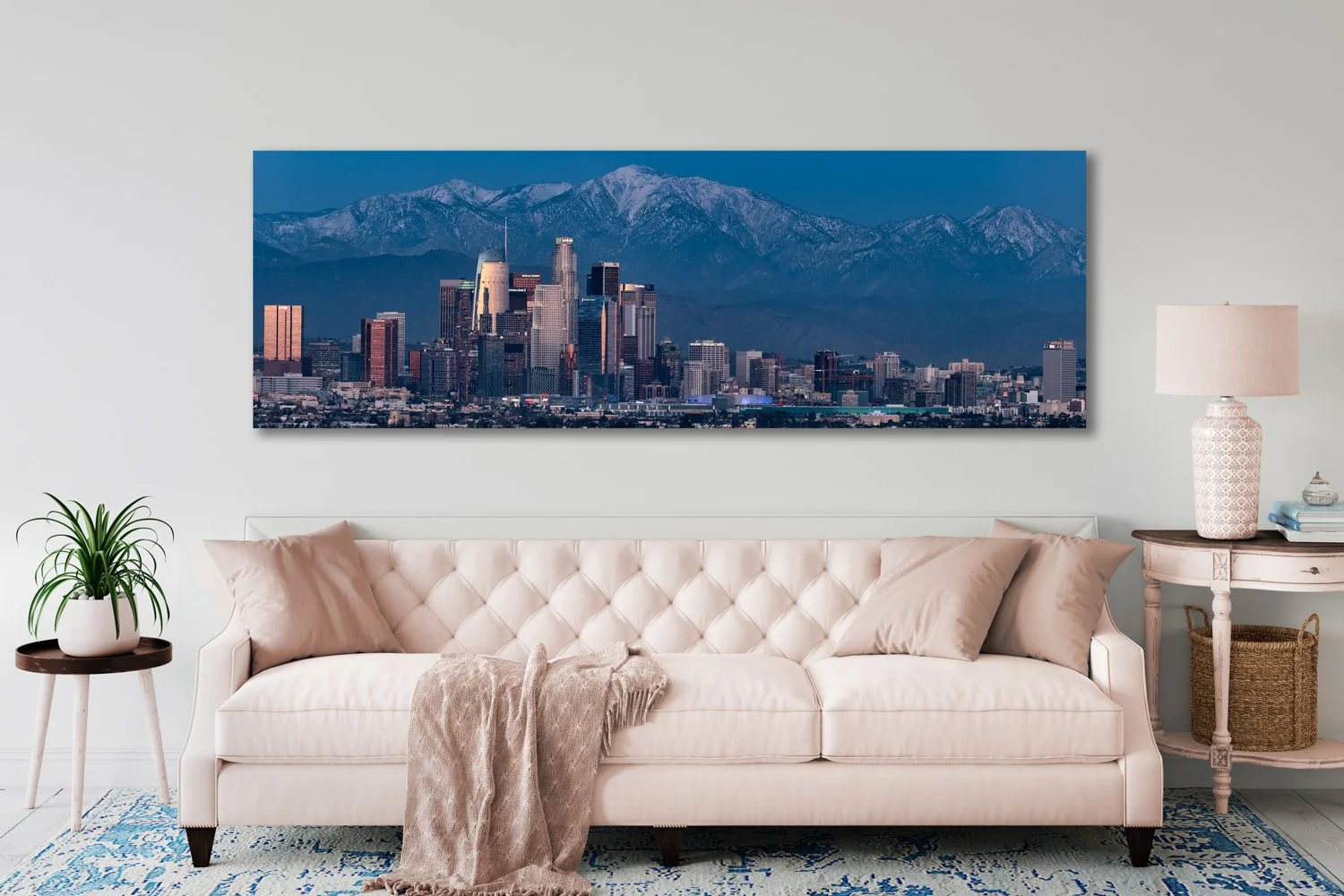 Elegant living room with panoramic 'LA Twilight' wall art from TomsWorldCollection, depicting Downtown Los Angeles against the San Gabriel Mountains during sunset, above a chic cream tufted sofa.